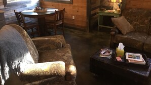 A cozy cabin interior with a wooden dining table, two chairs, a sofa, and a coffee table with various items. - Rustic luxury deep in the heart of Texas  (Hamilton)