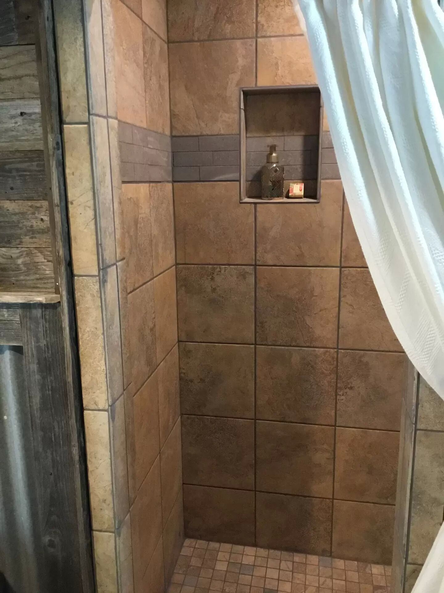 A shower area with tiled walls and a small shelf with toiletries.