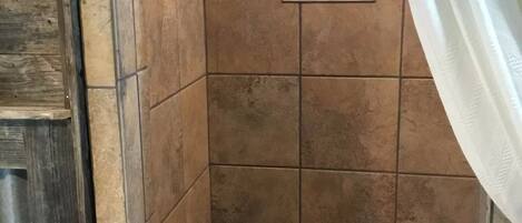 A shower area with tiled walls and a small shelf with toiletries.
