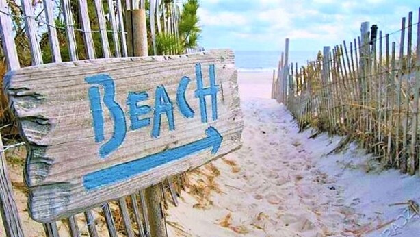 Un panneau en bois portant le mot « Plage » et une flèche pointant vers la droite, indiquant la direction à suivre pour se rendre à la plage.