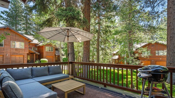 Een houten terras met een bank, een tafel en een parasol.