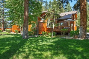 A wooden cabin with a deck, surrounded by trees and a well-maintained lawn.