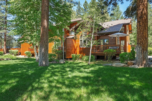 A wooden cabin with a deck, surrounded by trees and a well-maintained lawn.