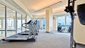 Ein Fitnessstudio mit Laufbändern, Ergometer und Rudergeräten, großen Fenstern und Blick aufs Meer.