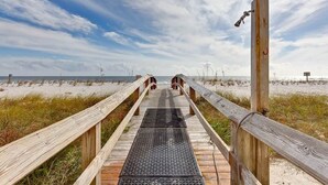 Ein hölzerner Steg führt zu einem Strand unter blauem Himmel.