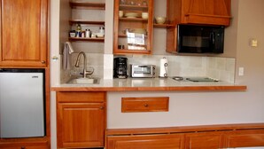 A compact kitchen with wooden cabinets, a built-in microwave, a toaster, and a coffee maker. - Finely Crafted Studio Apartment In The Heart Of Old Town (Fort Collins)