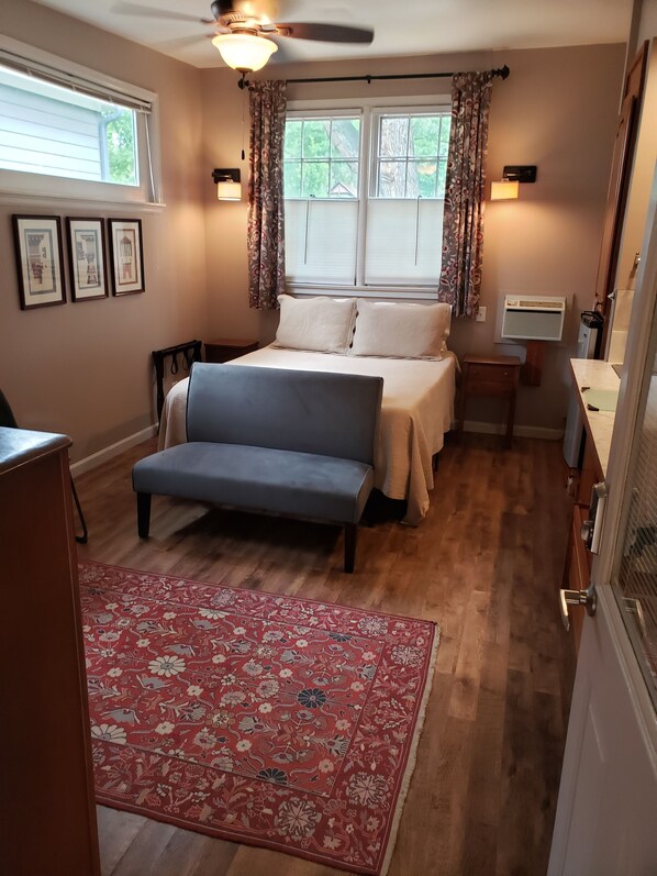 A bedroom with a bed, a desk, a chair, a ceiling fan, and a window with curtains.