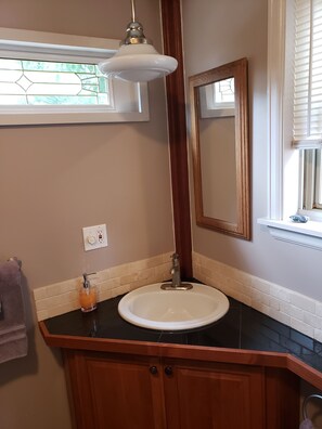 A bathroom with a white sink, wooden vanity, a mirror, and a hanging light fixture.