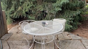 A round metal table with four chairs in a garden area with a large evergreen tree in the background. - Finely Crafted Studio Apartment In The Heart Of Old Town (Fort Collins)