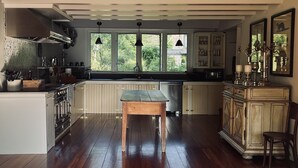 A spacious kitchen with a wooden dining table, a built-in oven, and a view of the outdoors through large windows. -  Catskills Sanctuary  (Delancey)