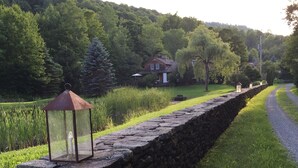 A stone wall with a lantern, a grassy path, and a house in the background. -  Catskills Sanctuary  (Delancey)