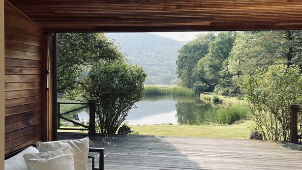 A wooden deck with a sofa and chairs, overlooking a lake and forested hills. -  Catskills Sanctuary  (Delancey)