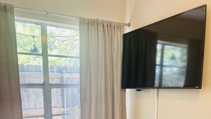 A room with two yellow armchairs, a small round table, a flat-screen TV mounted on the wall, and a large window with curtains.