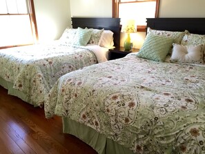Two double beds with floral bedding, wooden headboards, and bedside tables with lamps.
