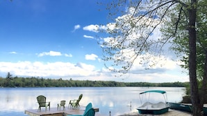 A lakeside deck with chairs and a table, a covered boat, and a dock extending into the water.