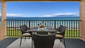Ein Balkon mit Esstisch, der Blick auf ein klares, blaues Meer und entfernte Berge bietet.