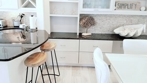 Une cuisine moderne dotée d’un îlot central, de meubles blancs et d’un pare-feu avec l’inscription « SIMPLIFY ».