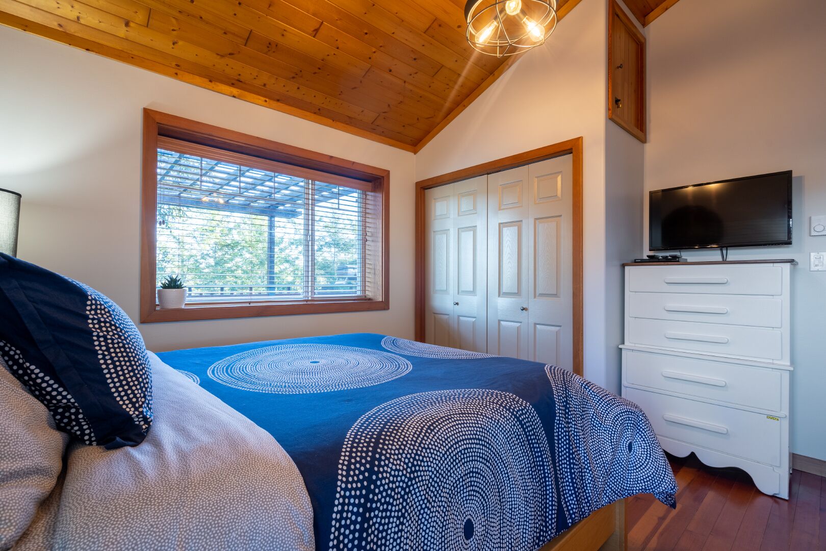 A bedroom with a bed, a dresser, a television, and a window with blinds.