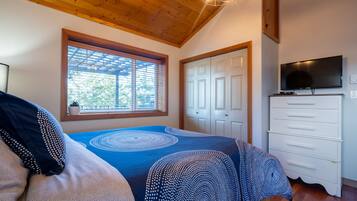 A bedroom with a bed, a dresser, a television, and a window with blinds.