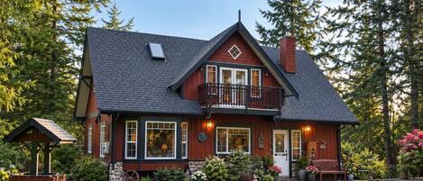 A two-story house with a balcony, surrounded by a well-maintained garden and tall trees.