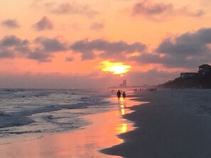 Une plage au coucher du soleil, avec des personnes se promenant le long du rivage.