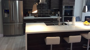 Una cocina moderna con armarios oscuros, electrodomésticos de acero inoxidable, una isla central con taburetes altos e iluminación colgante.