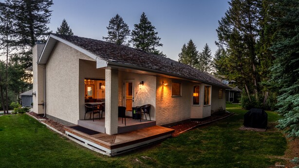 Eingeschossiges Haus mit überdachter Veranda, einer kleinen Terrasse und einem gepflegten Rasen.