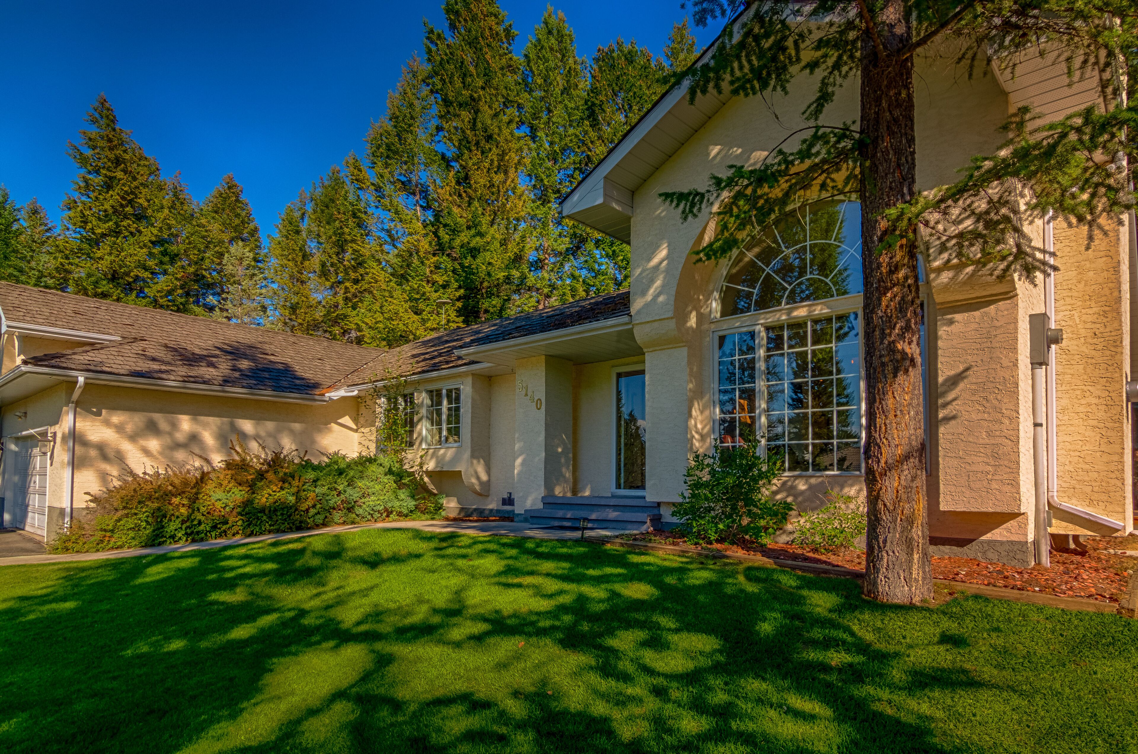A two-story house with a well-maintained lawn, a garage, and a large window overlooking the yard.