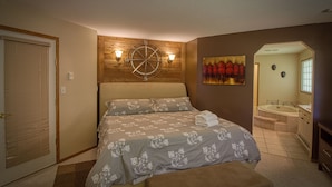 Ein Schlafzimmer mit einem Bett, einer Holzwanduhr, einem Gemälde und einem durch eine offene Tür einsehbaren Badezimmer.