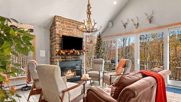 A cozy living room with a fireplace, comfortable seating, and a large window overlooking a forest. - Summer DISCOUNT Belleayre Mountain House, Catskills (Fleischmanns Heights)
