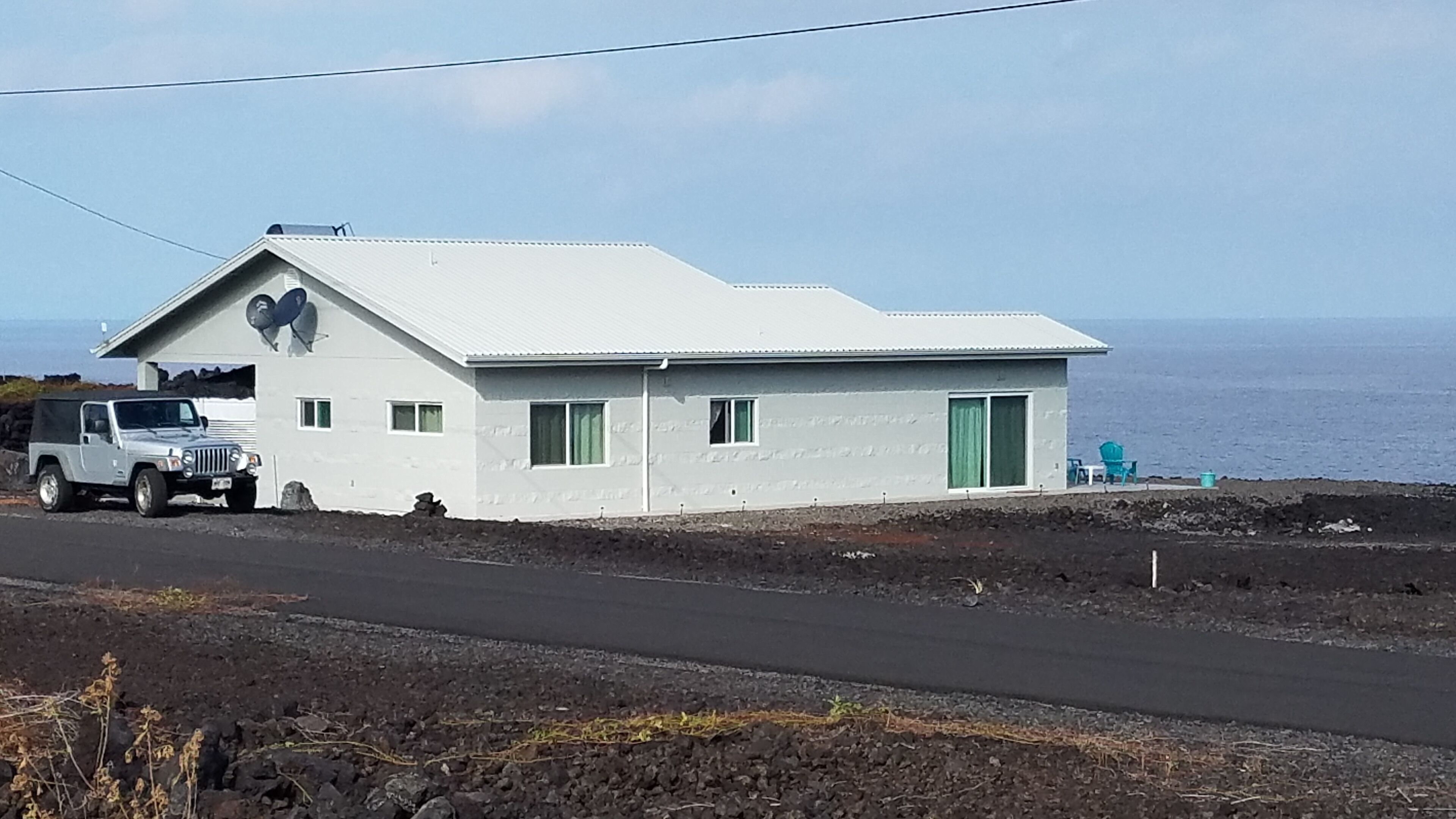 A white building with a heart-shaped window, a parked vehicle, and a view of the ocean.