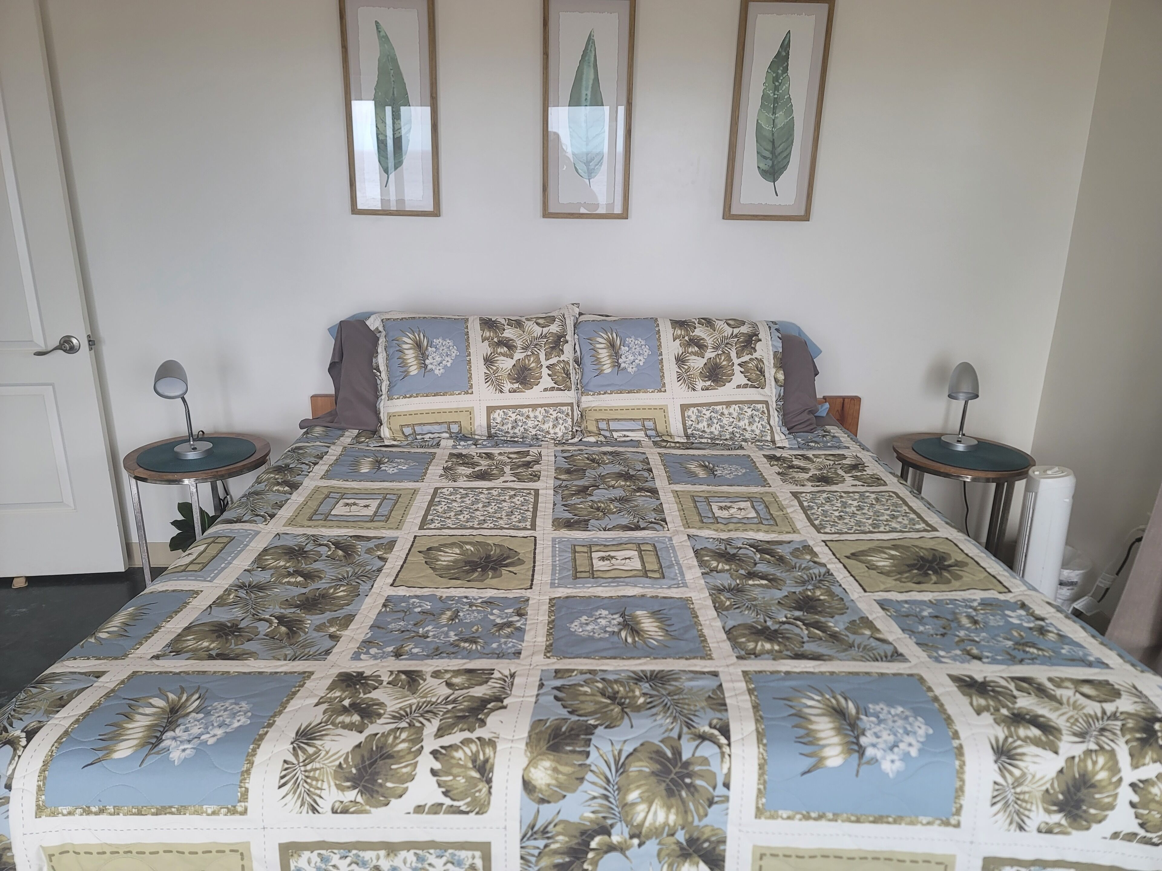 Un dormitorio con una colcha de estampado floral, dos mesitas de noche con lámparas y tres láminas botánicas enmarcadas en la pared.