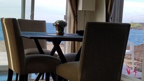 Un comedor con una mesa y sillas, una planta en maceta y vista al mar.