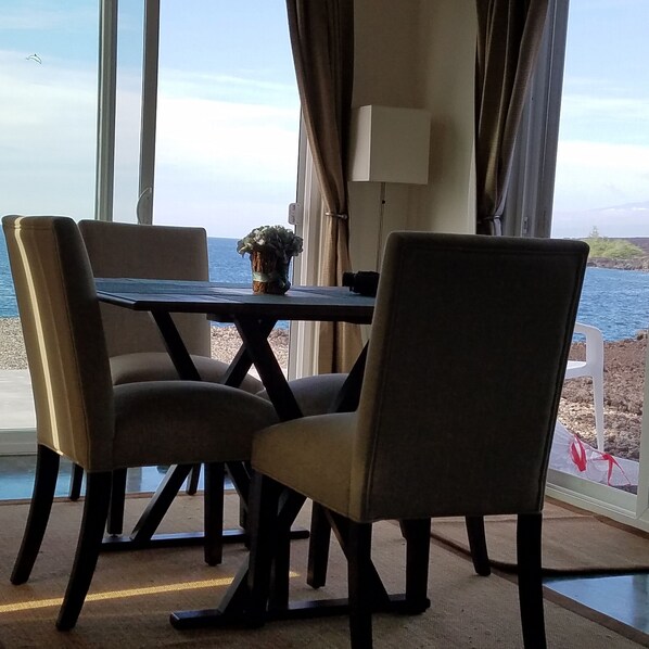 Un comedor con una mesa y sillas, una planta en maceta y vista al mar.