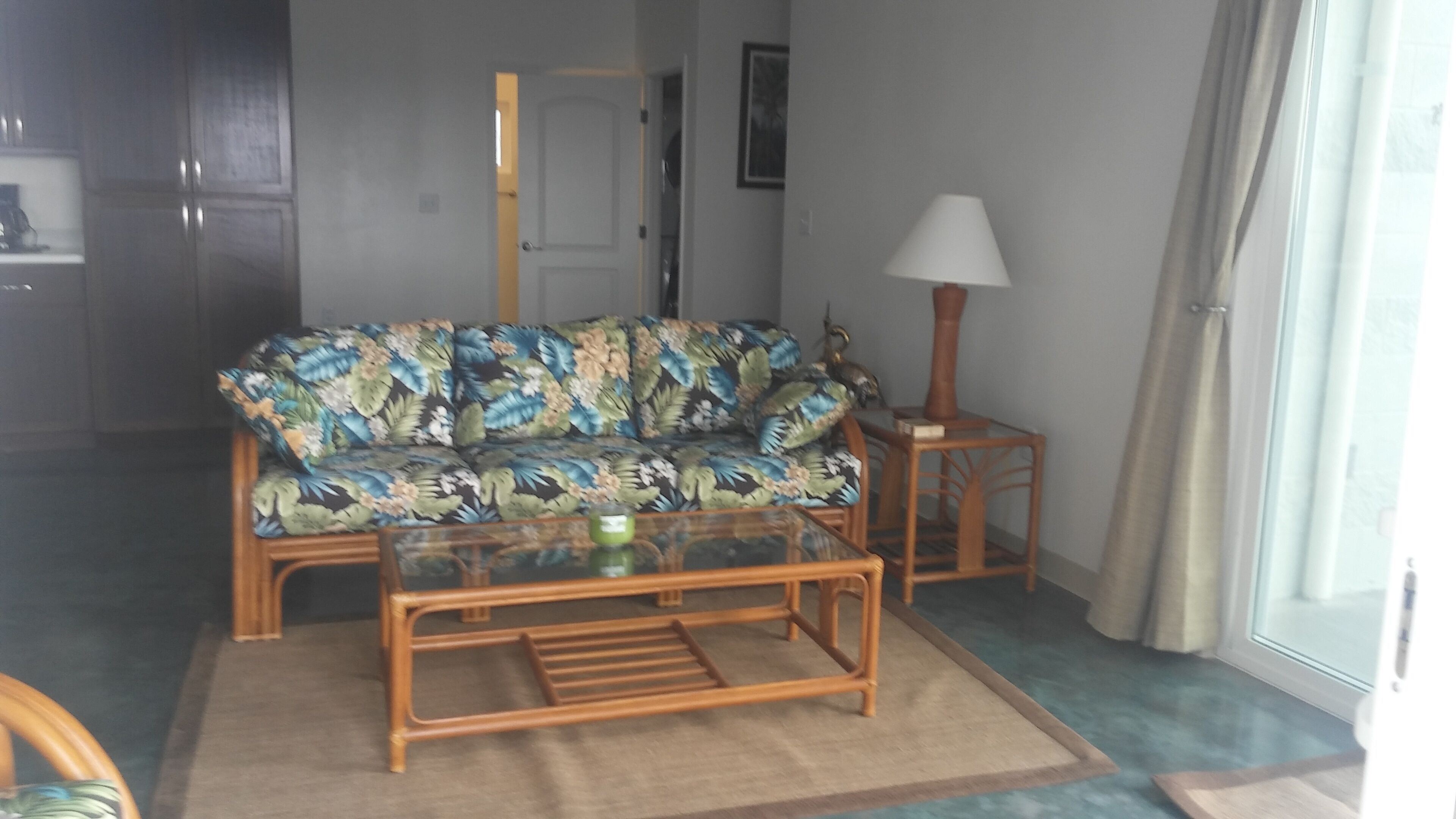 Una sala de estar con un sofá, una mesa de centro de vidrio, una lámpara y vistas por una ventana.
