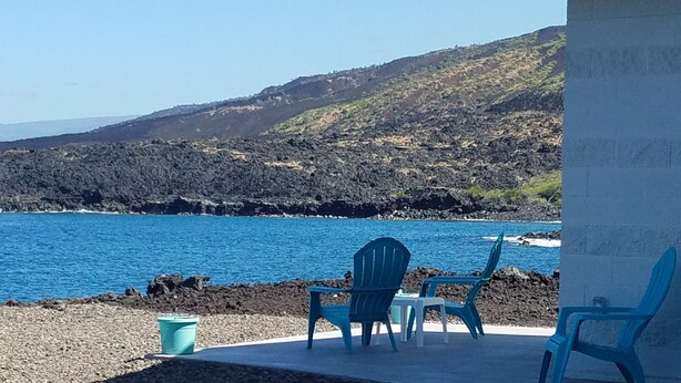 Un patio con dos sillas y un balde, con vista a una costa rocosa y un mar azul cristalino.