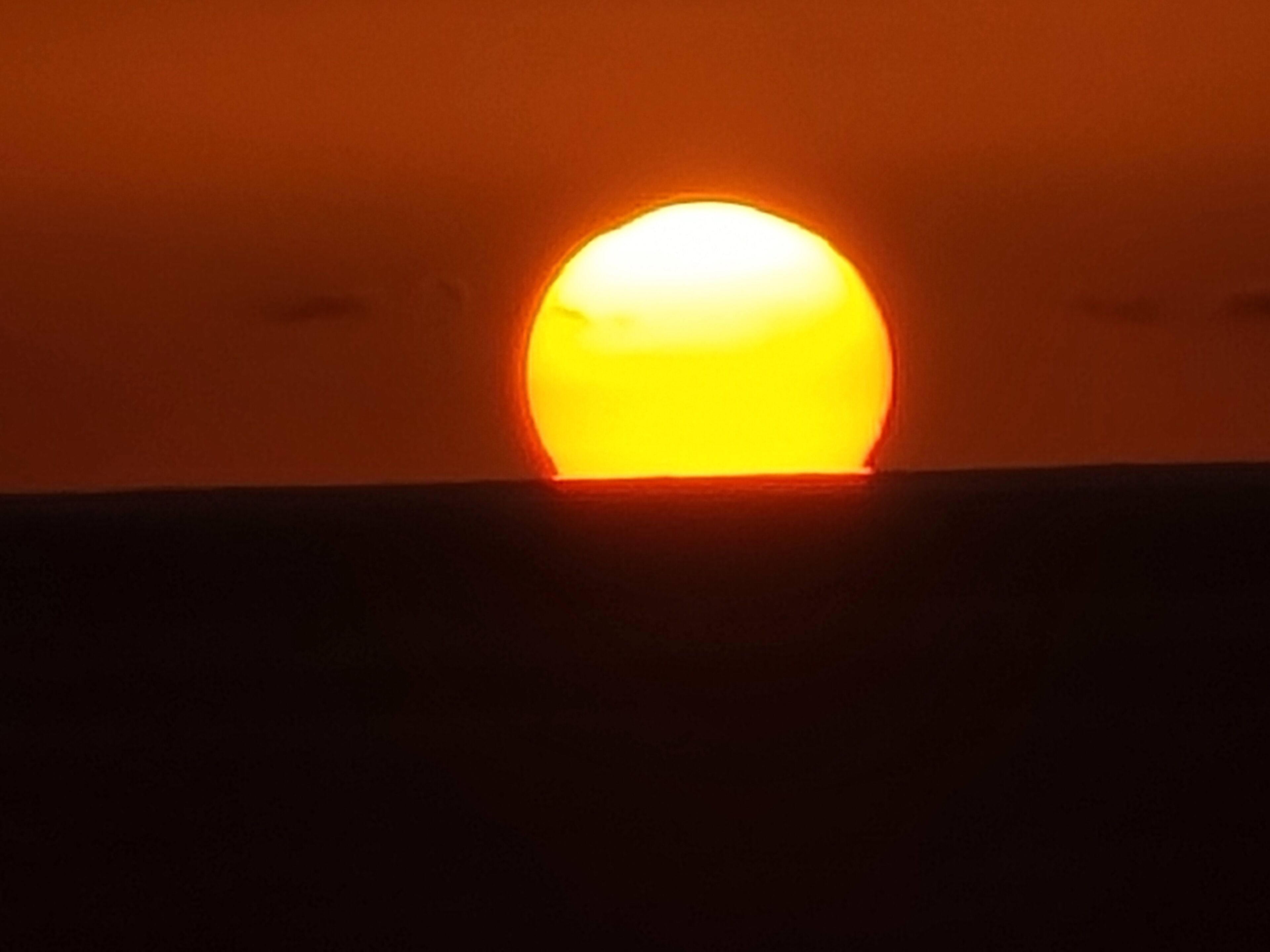 A sunset with a sun partially obscured by clouds.