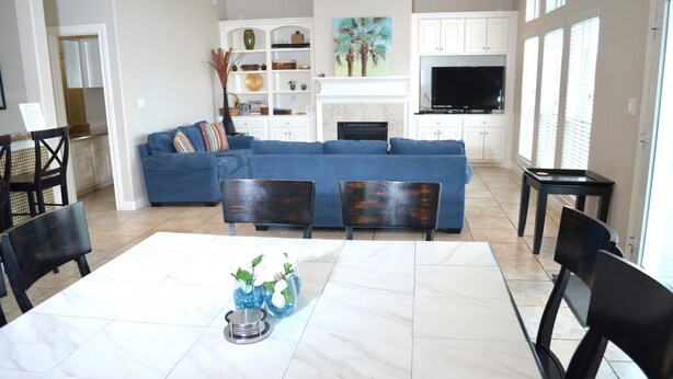 A spacious living room with a blue sofa, a dining table with chairs, and a fireplace. - Pirates Beach - Chez Antoine - Beautiful, Four Bedroom, Three Bath (Galveston)
