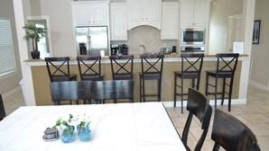 A kitchen with white cabinets, a central island with bar stools, and a dining table with chairs. - Pirates Beach - Chez Antoine - Beautiful, Four Bedroom, Three Bath (Galveston)