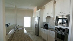 A modern kitchen with white cabinets, granite countertops, stainless steel appliances, and a window providing natural light. - Pirates Beach - Chez Antoine - Beautiful, Four Bedroom, Three Bath (Galveston)