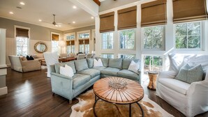 A spacious living room with a sectional sofa, a round coffee table, and a large window with multiple views. - Coastal Chic Home with Exquisite Design, Outdoor Living, Golf Cart & Watercolor Beach Club Access (Santa Rosa Beach)