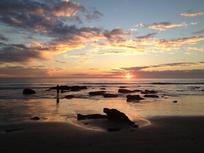 Une plage au coucher du soleil, avec des rochers et une personne debout.