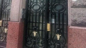 En svart, smidesjärnsgrind med detaljerade ornament och en plakett, placerad i en byggnad av sten. På höger sida sitter en nummerskylt med siffran ’768’.