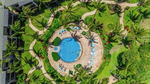 Vue aérienne d’un complexe hôtelier doté d’une piscine centrale, entourée de chaises longues et de palmiers.