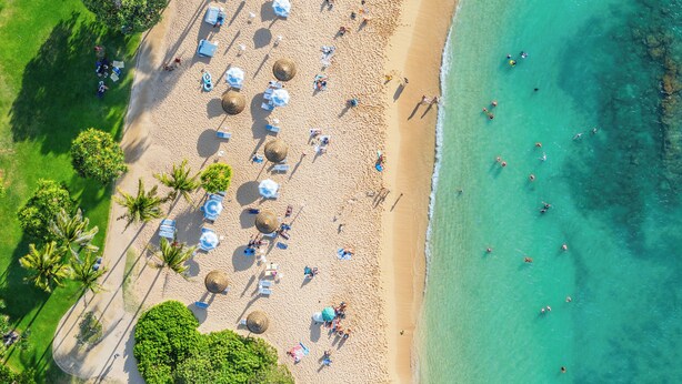Une vue aérienne d’une plage avec des parasols, des palmiers et des personnes.