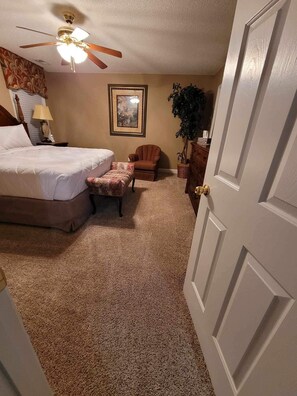 A bedroom with a bed, a chair, a desk, a ceiling fan, a framed picture, and a door.