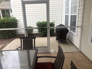 A patio with a glass table and chairs, a barbecue grill, and a covered area with a view of the backyard.