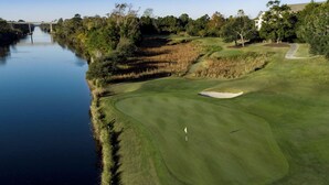 Un campo da golf con una distesa d'acqua su un lato, un ponte sullo sfondo e un edificio alla destra.