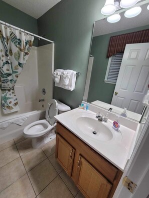 A bathroom with a toilet, sink, and shower. There are towels hanging on the wall and a mirror above the sink.