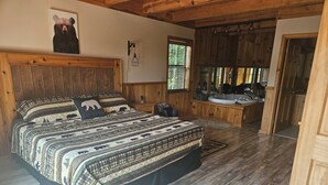 Een slaapkamer met een groot bed, een houten hoofdbord, een nachtkastje, een badkamer met een badkuip, een wastafel en een spiegel.